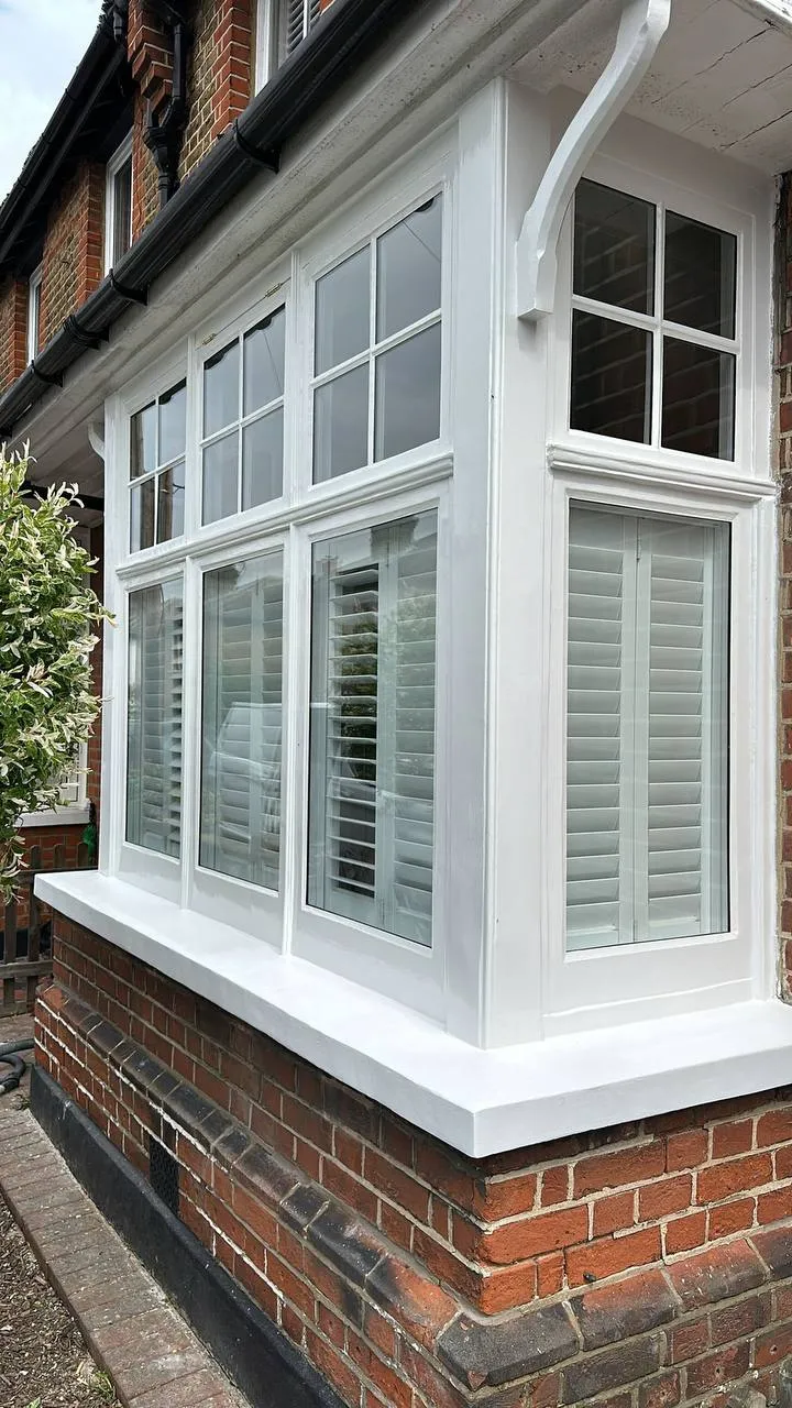 Beautifully restored white timber bay window with plantation shutters and glossy paintwork on a brick house