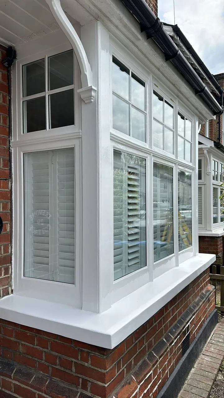 Restored white timber bay window with shutters and crisp gloss paint on a red brick Edwardian house