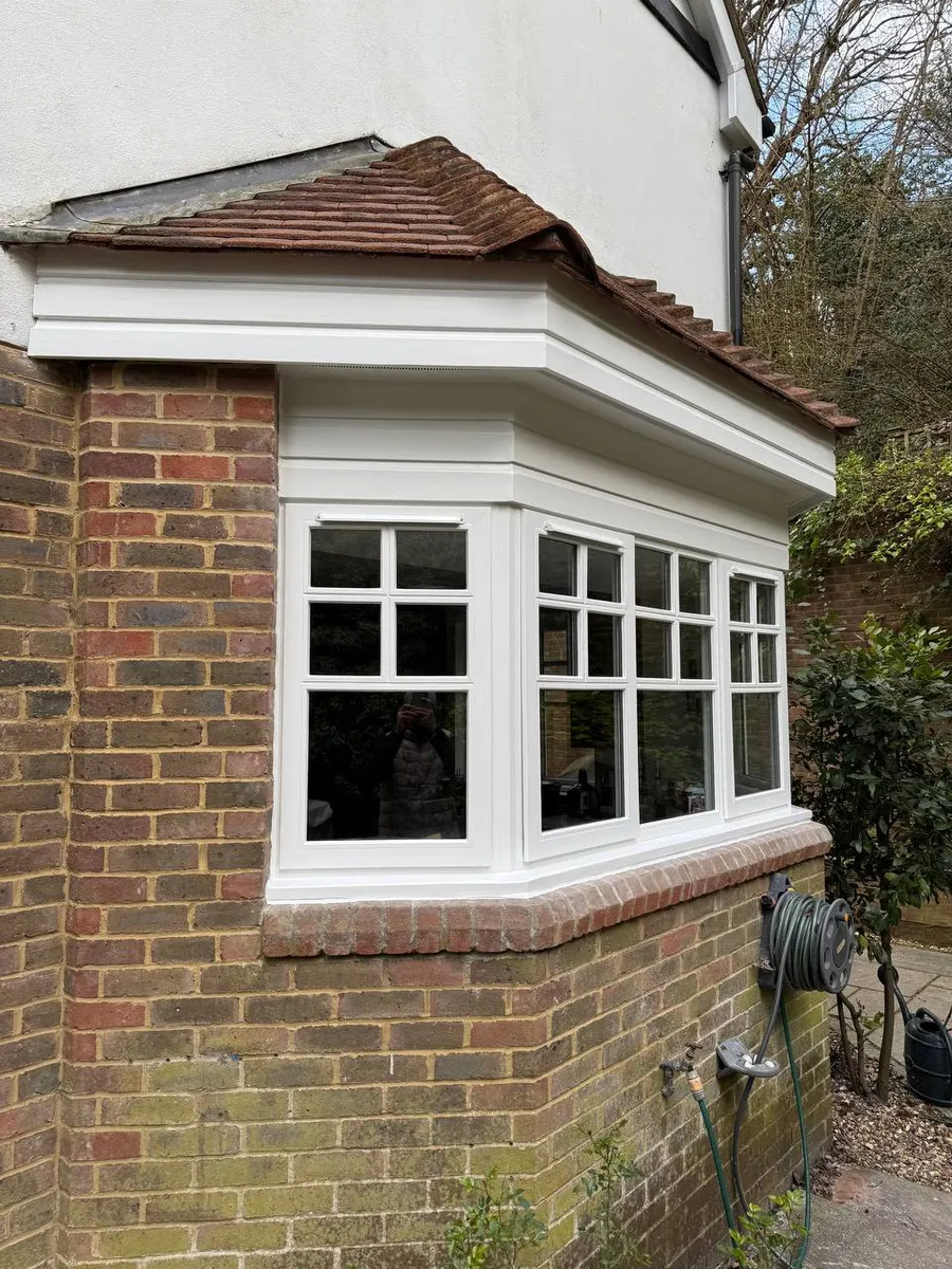 Restored white timber corner bay window with a tiled roof on a brick house, Surrey