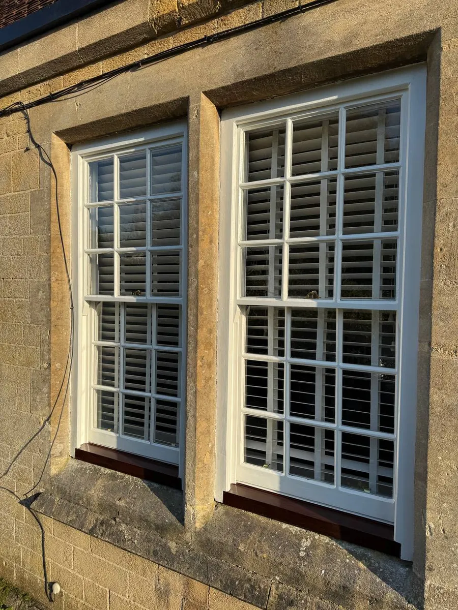 Freshly restored multi-pane sash windows with new hardwood sills on a stone period property in golden light