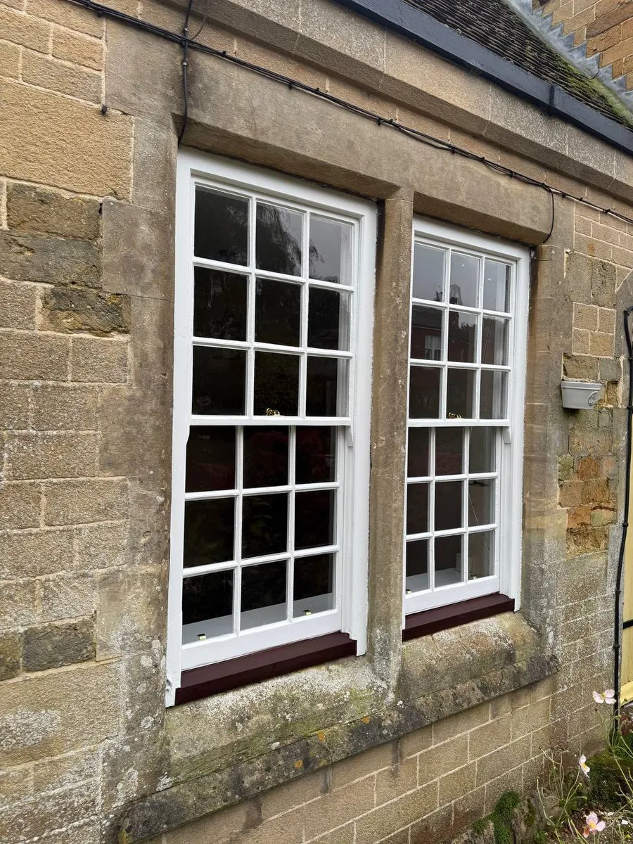 Beautifully restored Georgian sash windows with white frames and oxblood-painted sills on a stone cottage