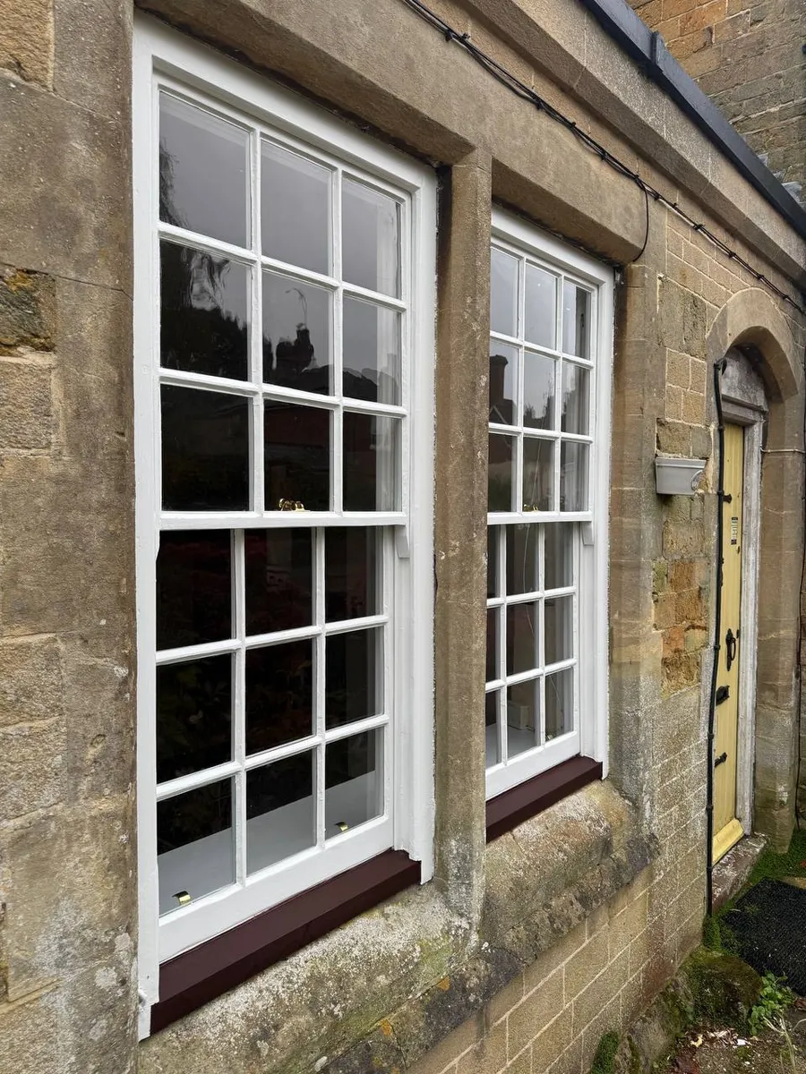 Restored multi-pane sash windows with oxblood sills next to a stone arched doorway on a period cottage