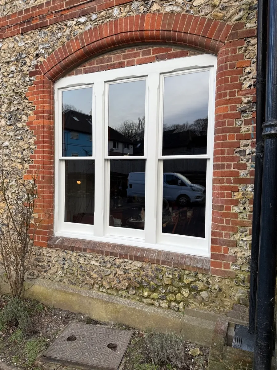 Freshly restored white timber casement window set in a flint and red-brick period wall