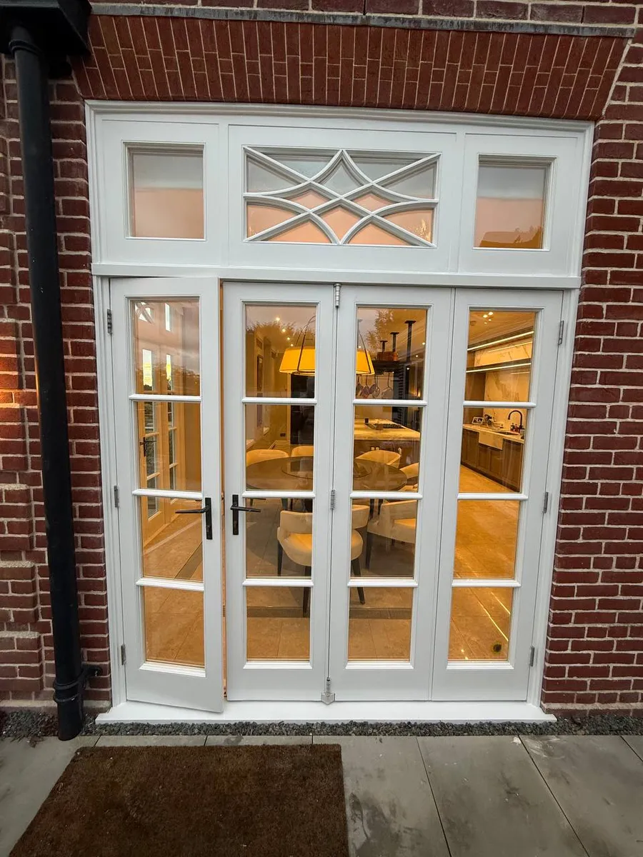 White timber french doors with side lights and a decorative astragal fanlight glowing at dusk