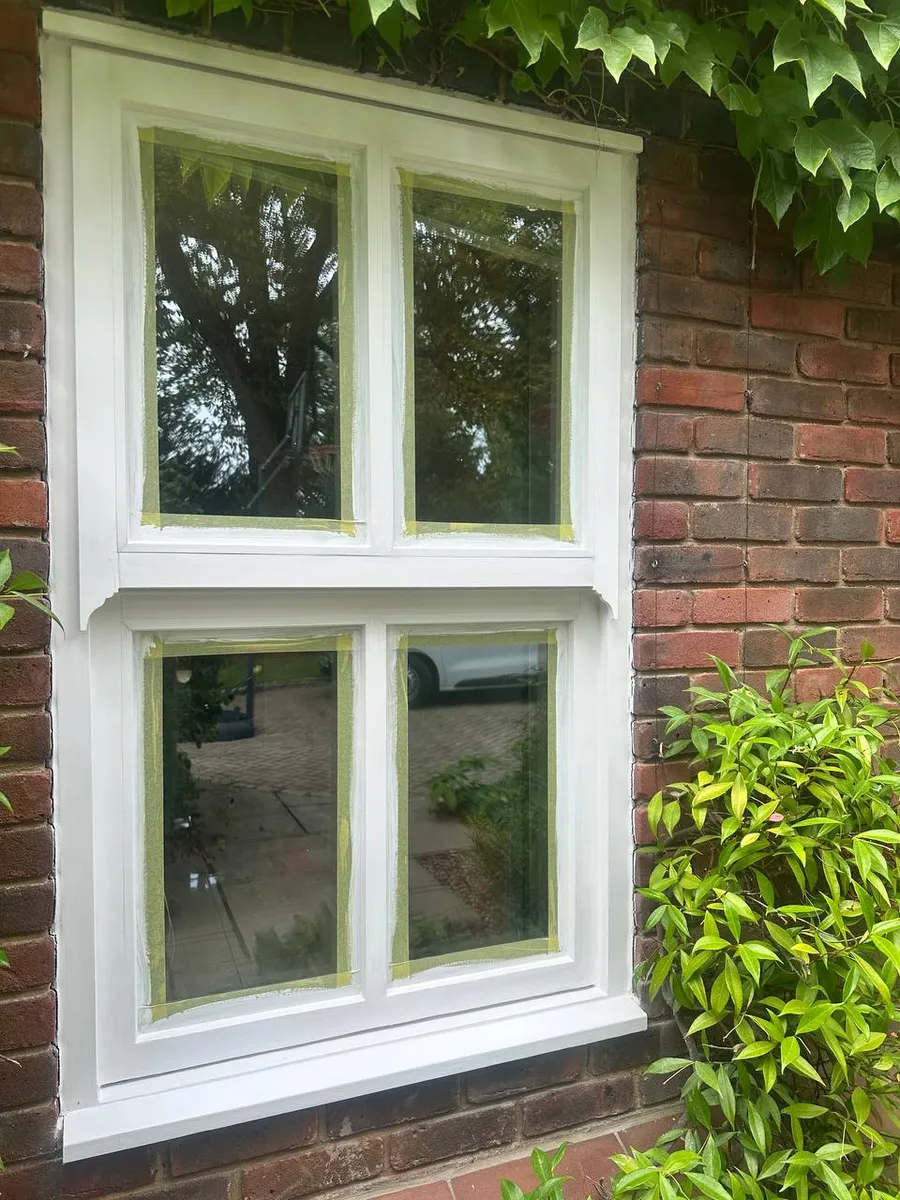 Freshly painted bright white timber sash window with masking tape on the glass on a brick wall